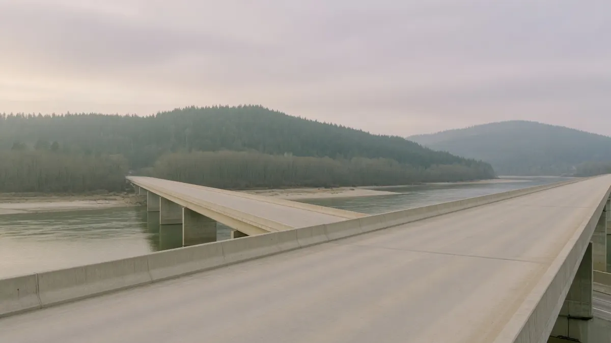 Pusty betonowy most autostradowy nad szeroką rzeką i zalesione wzgórza w porannej mgle