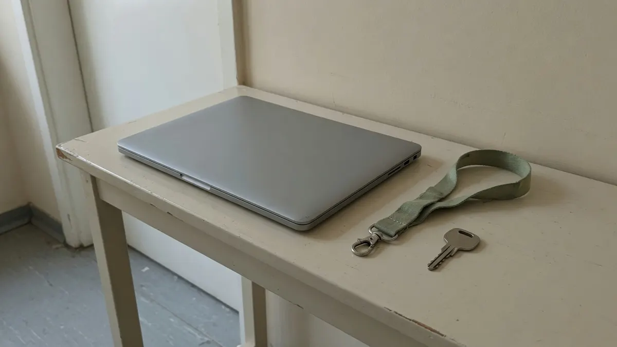 Zamknięty srebrny laptop, zielona smycz i klucz na jasnej konsoli w przedpokoju