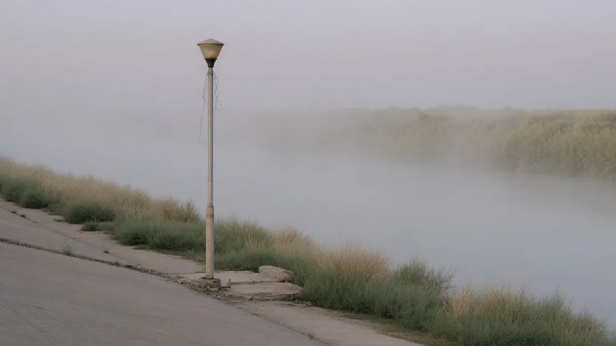 Samotna latarnia na pustym nadrzecznym bulwarze spowitym gęstą poranną mgłą